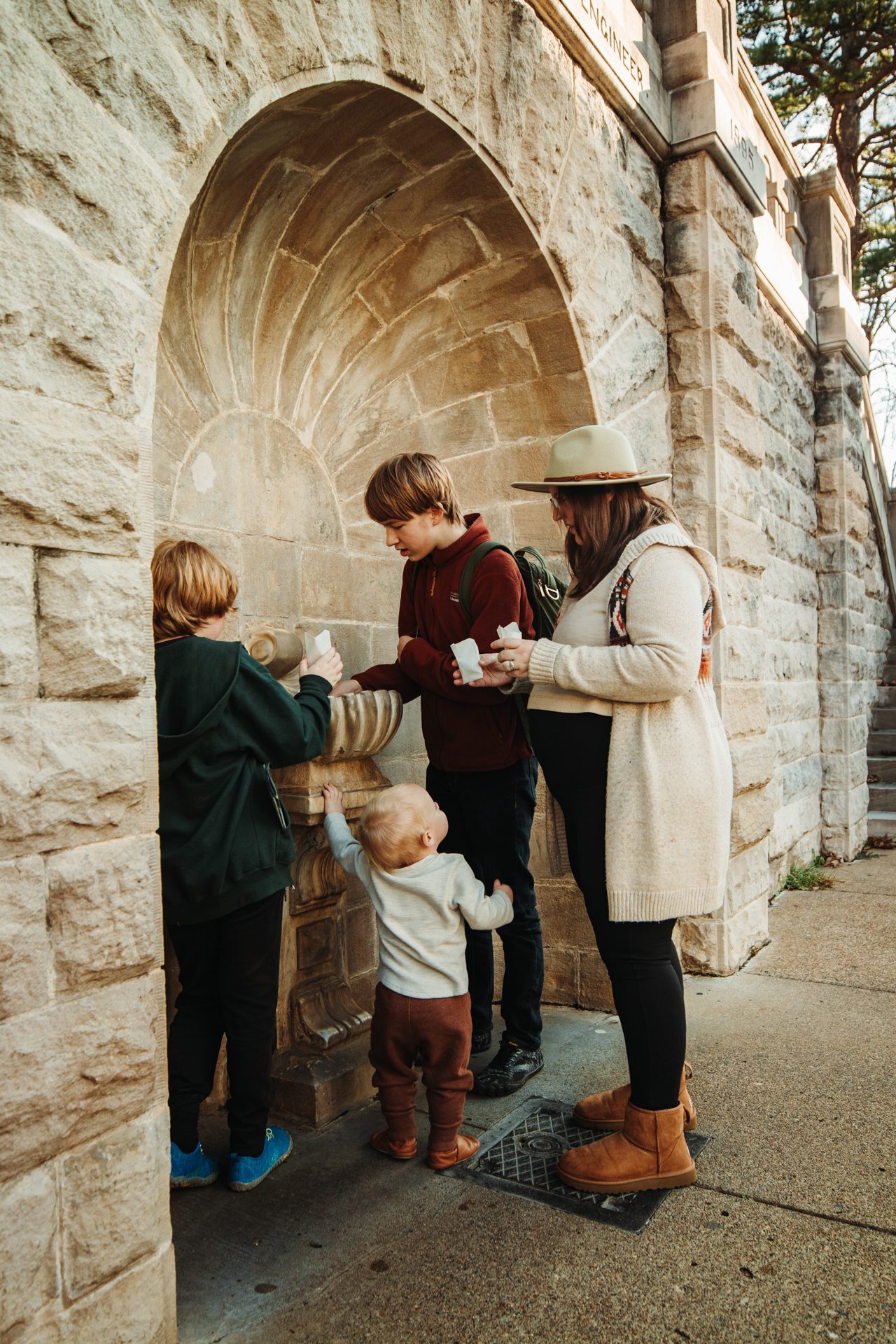 Four people collecting water from a spring fountain